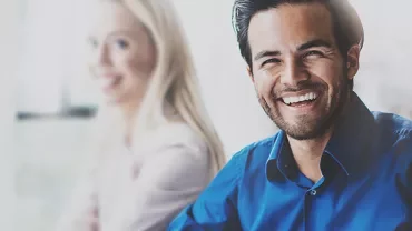 Persona sorridente con camicia blu in un ambiente professionale.