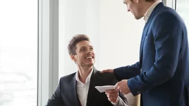 Colleghi in ufficio, uno seduto sorride mentre riceve una lettera.