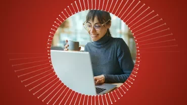 Persona sorride mentre lavora al computer con una tazza.