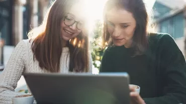 Persone sorridenti che lavorano su un portatile all'aperto.