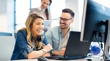 Persone che ridono insieme al computer in ufficio.