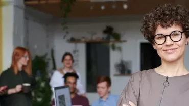 Persona sorridente in ufficio con colleghi sullo sfondo.