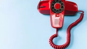 Vecchio telefono rosso a disco su sfondo azzurro.