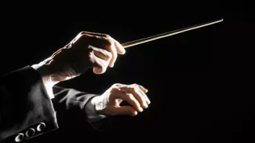 Mani che dirigono un'orchestra con la bacchetta su sfondo nero.