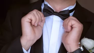 Persona che sistema un papillon nero su una camicia bianca.