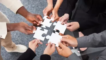Mani diverse che assemblano pezzi di puzzle.