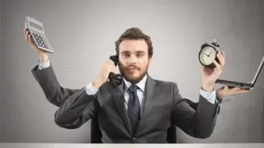 Persona multitasking con calcolatrice, telefono, orologio e laptop.