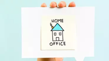 Disegno di una casa con tetto blu su un foglio bianco tenuto da una mano.