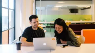 Due persone che sorridono mentre guardano un laptop in ufficio.
