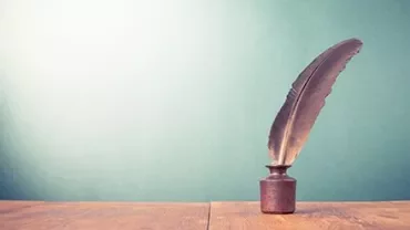 Piuma da scrittura in un calamaio su un tavolo di legno.