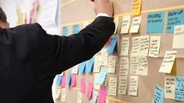 Persona scrive su una lavagna piena di post-it colorati.