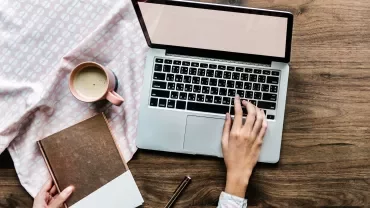 Mano su laptop con tazza di caffè su tavola di legno