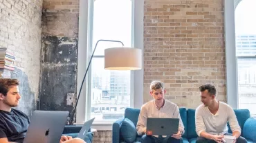 Persone sedute su un divano con computer portatili.