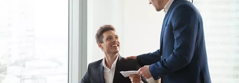 Colleghi in ufficio, uno seduto sorride mentre riceve una lettera.