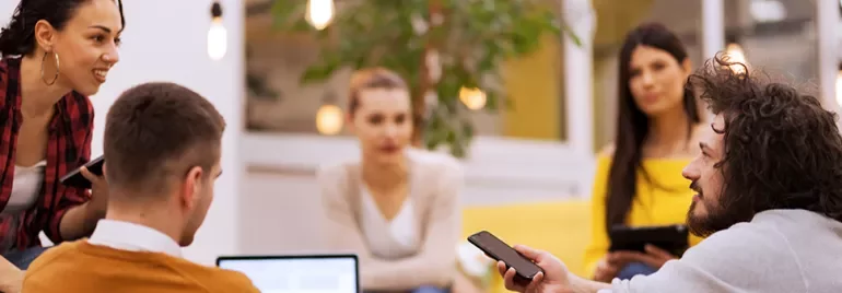 Gruppo di persone riunite in ufficio con dispositivi tecnologici.