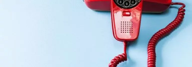 Vecchio telefono rosso a disco su sfondo azzurro.
