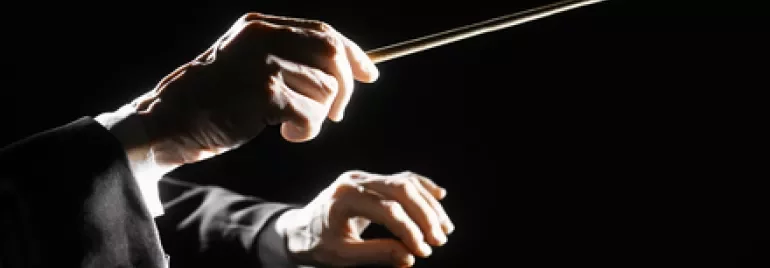 Mani che dirigono un'orchestra con la bacchetta su sfondo nero.