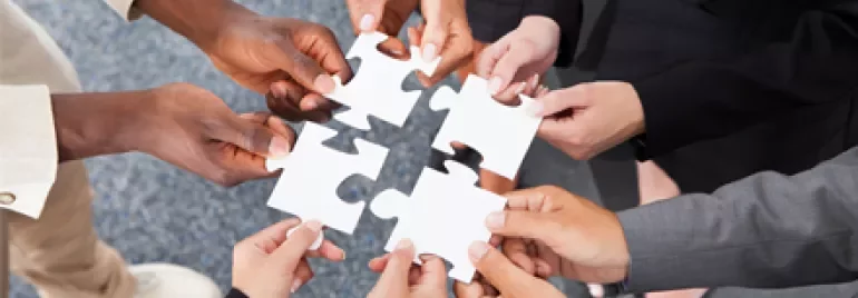 Mani diverse che assemblano pezzi di puzzle.