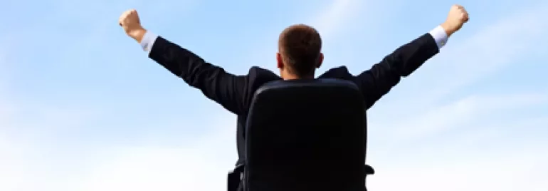 Persona seduta all'aperto su sedia da ufficio, braccia alzate.