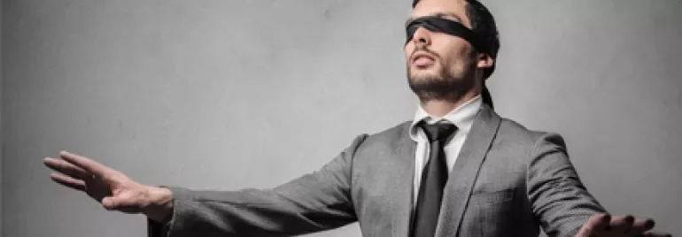 Persona in abito, bendata, con le braccia tese in avanti.