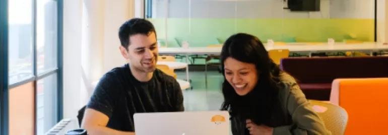 Due persone che sorridono mentre guardano un laptop in ufficio.
