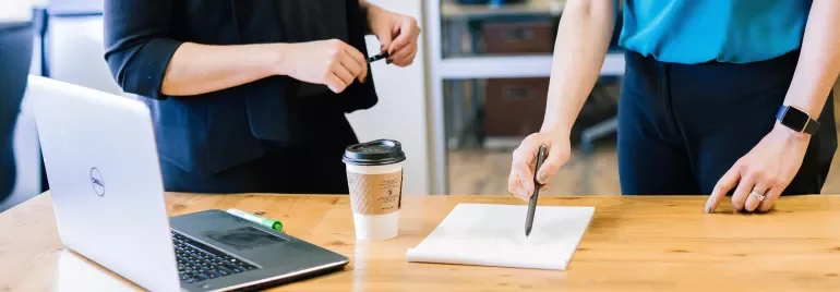 Due persone discutono accanto a un laptop e un blocco note su un tavolo.