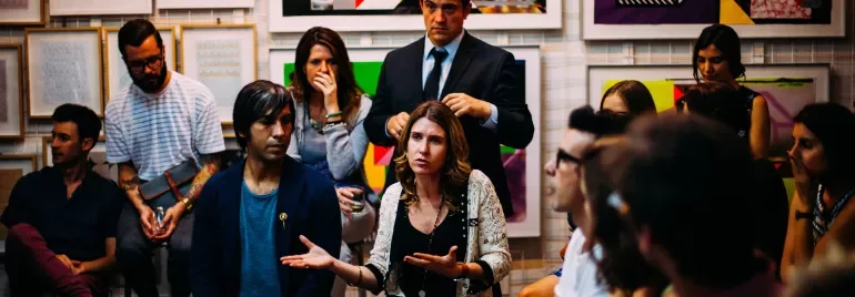 Persone sedute in una galleria d'arte con dipinti colorati sullo sfondo.