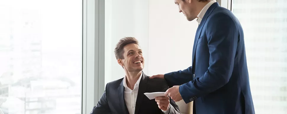 Colleghi in ufficio, uno seduto sorride mentre riceve una lettera.